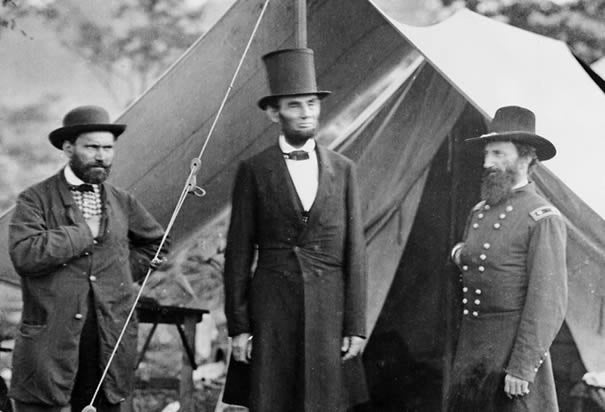 Historical black-and-white photograph of Abraham Lincoln, the 16th President of the United States. Depicts Lincoln in formal 19th-century attire, including his iconic stovepipe hat and beard. A symbol of leadership, the Civil War era, and the abolition of slavery.